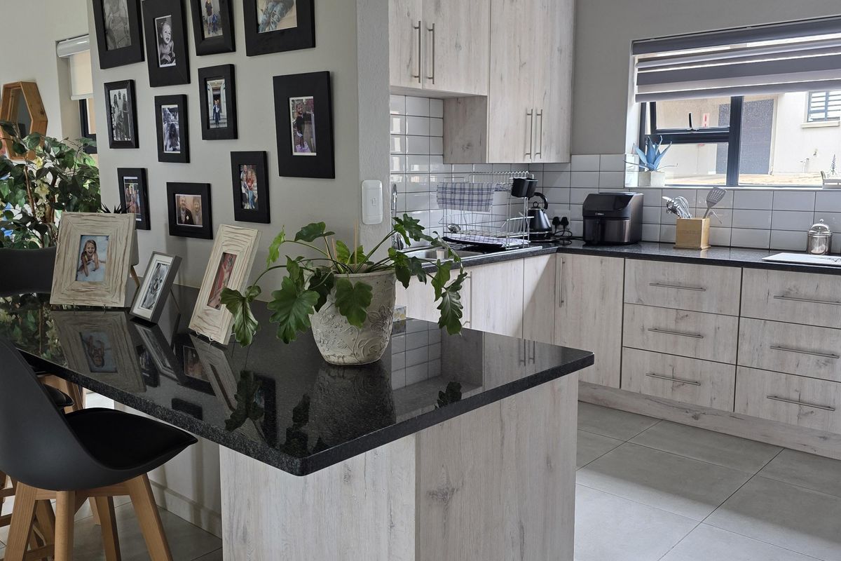 Modern kitchen featuring light wood-grain cabinetry, contrasting black granite countertops, a breakfast bar island, and tiled flooring under a vaulted ceiling.