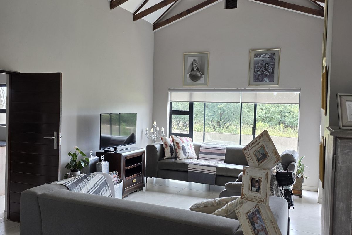 Spacious living room featuring high vaulted ceilings with exposed timber trusses, large windows, and tiled flooring.