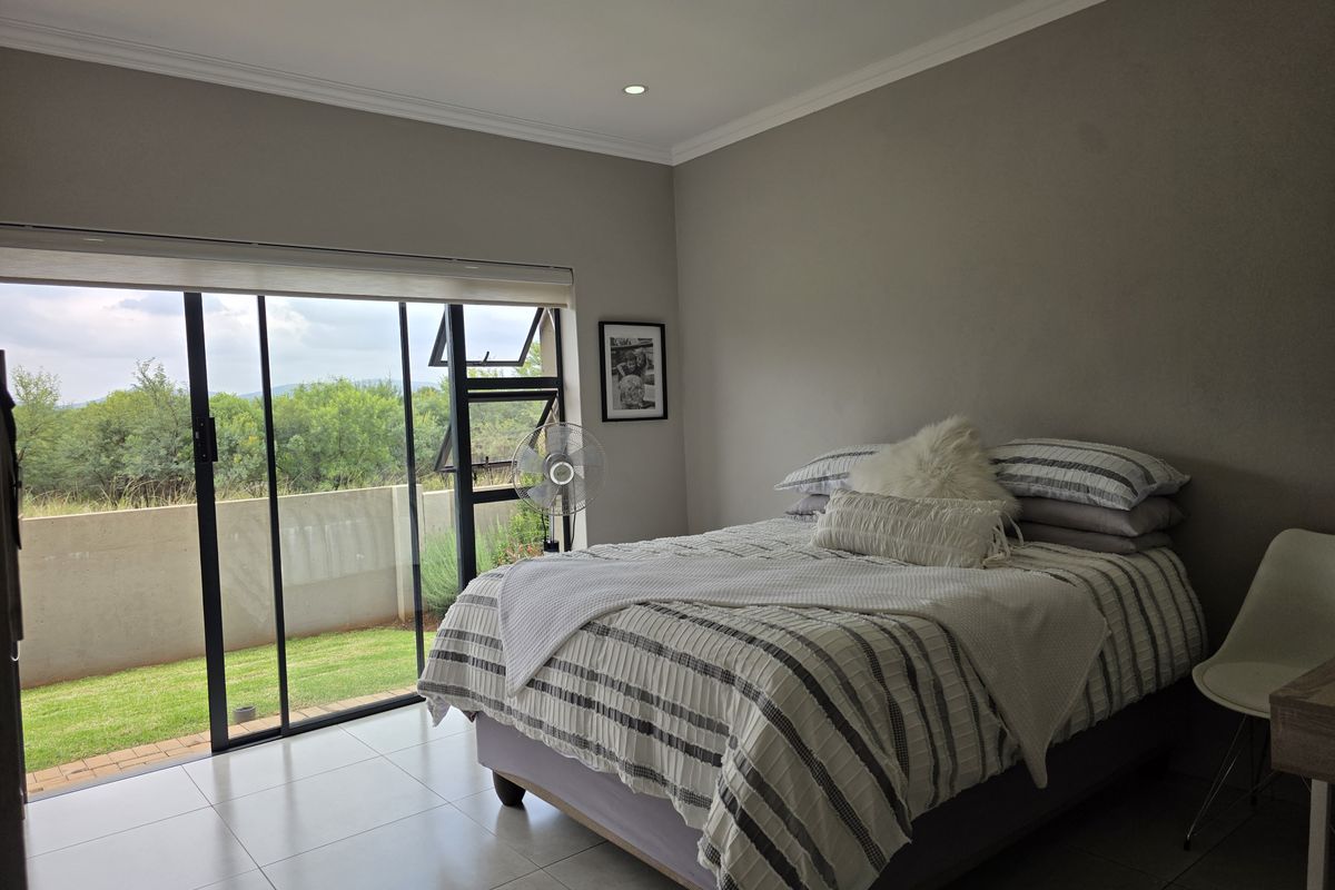 A bright bedroom featuring large sliding glass doors that open to a private garden area, complemented by neutral tiled flooring and recessed ceiling lighting.
