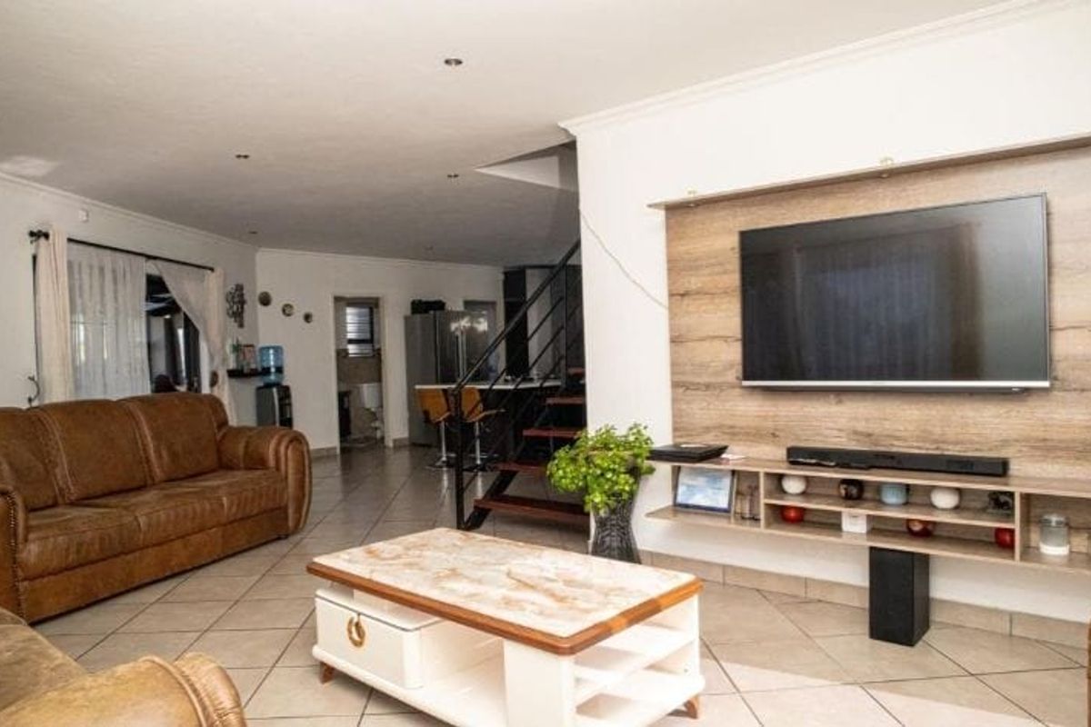 Open plan living area featuring tiled flooring, a built-in wooden media unit, and a staircase leading to the upper level.