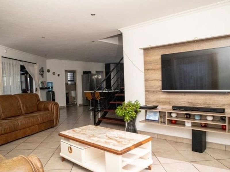Open plan living area featuring tiled flooring, a built-in wooden media unit, and a staircase leading to the upper level.