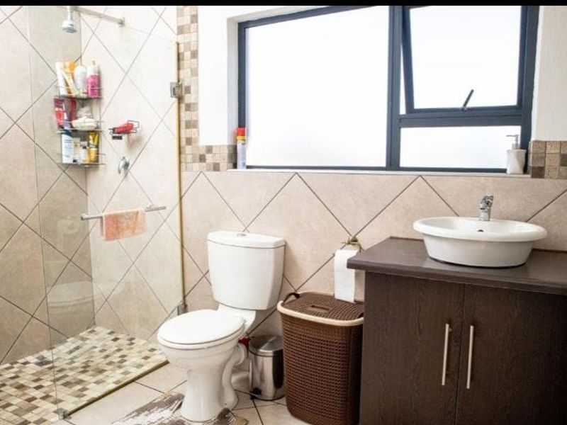 A functional bathroom featuring a glass-enclosed shower with mosaic tile accents, a vanity with a vessel sink, and a standard toilet.