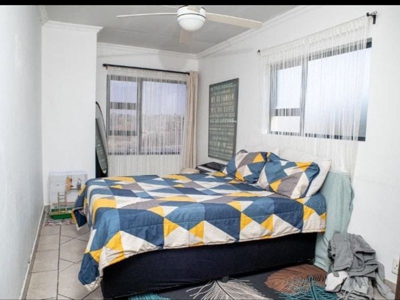 A functional bedroom featuring tiled flooring, dual windows for natural light, and a ceiling fan.