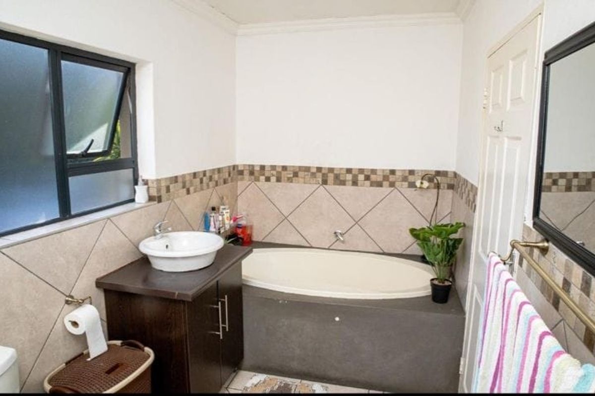 A functional bathroom featuring a built-in bathtub, a vessel sink vanity, and tiled wall accents with a window for natural light.