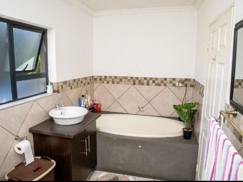 A functional bathroom featuring a built-in bathtub, a vessel sink vanity, and tiled wall accents with a window for natural light.