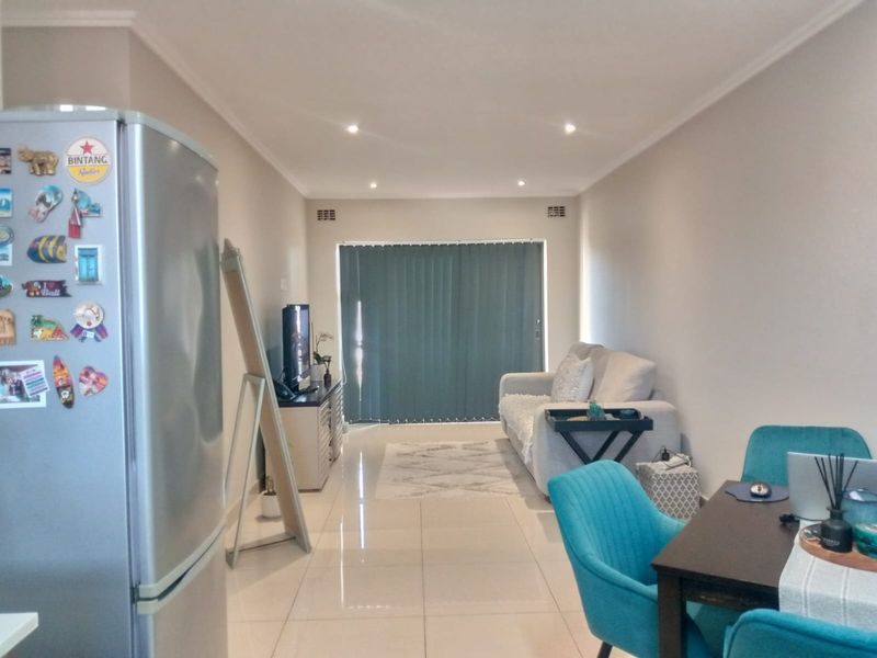 An open-plan living and dining area featuring tiled flooring, recessed ceiling lighting, and sliding glass doors with vertical blinds leading to an outdoor space.