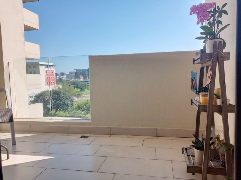 A bright, tiled balcony featuring a glass balustrade and solid wall, offering an open view of the surrounding neighborhood.