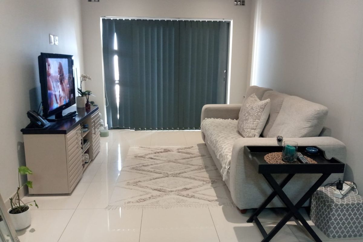 A well-maintained living room featuring tiled flooring and a large sliding glass door with vertical blinds, providing access to the exterior.