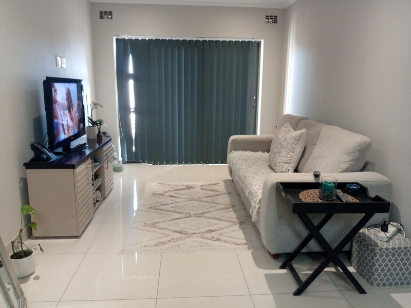 A well-maintained living room featuring tiled flooring and a large sliding glass door with vertical blinds, providing access to the exterior.