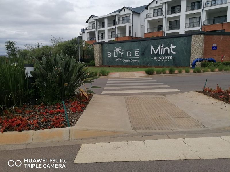 Street view of the entrance to The Blyde Crystal Lagoons complex, featuring a pedestrian crossing and modern multi-story apartment architecture.