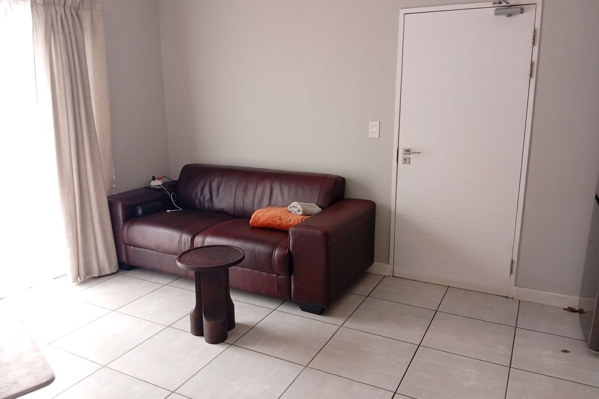 A living area featuring neutral wall tones, tiled flooring, and a functional door with a mounted closer.