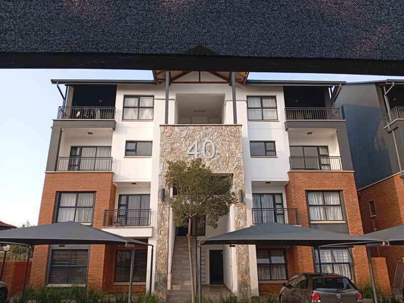 Front elevation of a multi-story apartment building featuring a stone-clad entrance, brick exterior, and covered parking bays.
