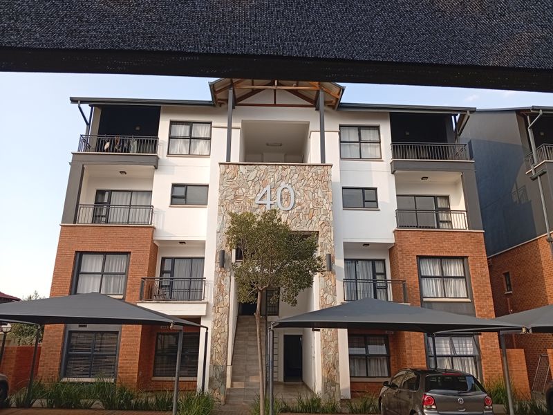 Front elevation of a multi-story apartment building featuring a stone-clad entrance, brick accents, and private balconies with metal railings.