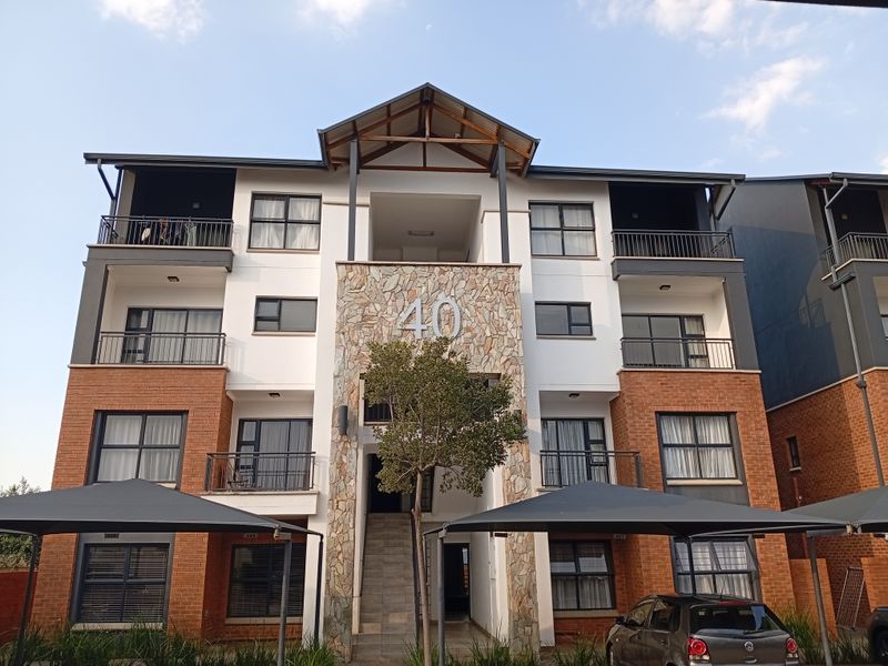Front elevation of a multi-story apartment building featuring a stone-clad entrance, face brick accents, and private balconies with metal railings.