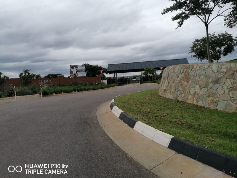 A view of the entrance road and security gatehouse leading to the property, featuring a stone retaining wall and landscaped verge.