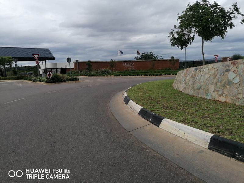 A view of the street approach and entrance area featuring paved roads, stone retaining walls, and landscaped surroundings.