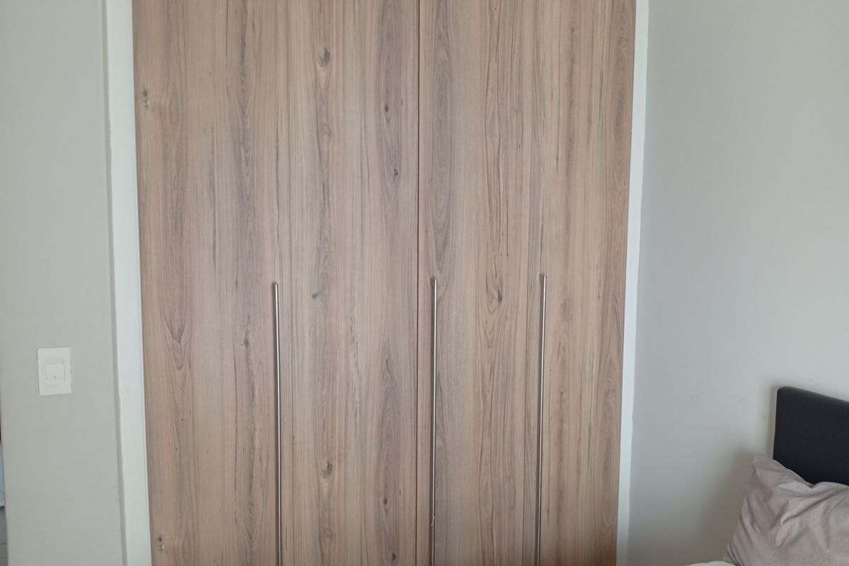 A bedroom featuring a modern, wood-grain finish built-in wardrobe with sleek vertical handles.