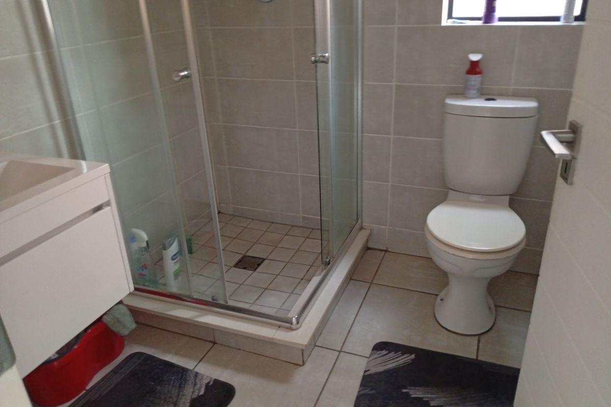 A functional bathroom featuring a glass shower enclosure, a white toilet, and a vanity cabinet with neutral wall and floor tiling.