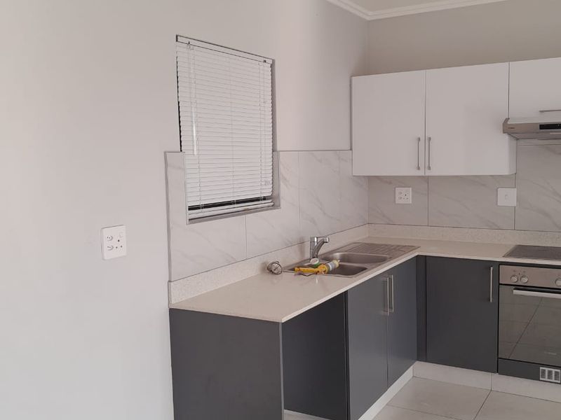 Modern kitchen featuring two-tone cabinetry, stone-look countertops, integrated stainless steel oven, hob, and extractor fan with tiled flooring.