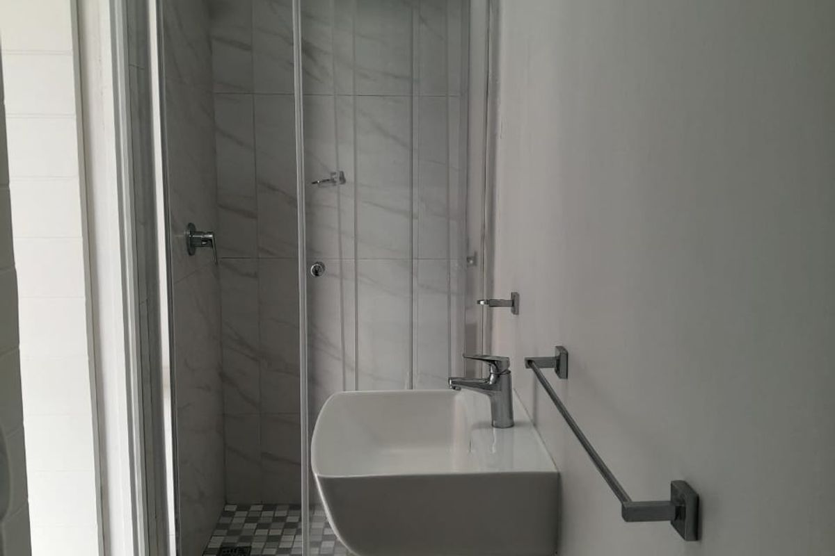 A modern bathroom featuring a pedestal basin, chrome fixtures, and a glass-enclosed shower with marble-look wall tiling.
