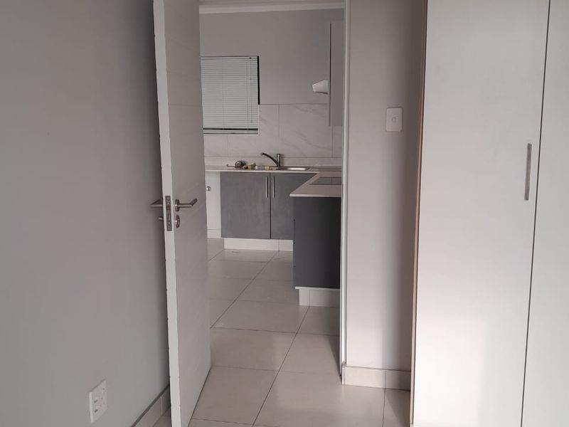 A view from a bedroom or hallway looking into a modern kitchen featuring grey cabinetry, tiled flooring, and built-in cupboards.