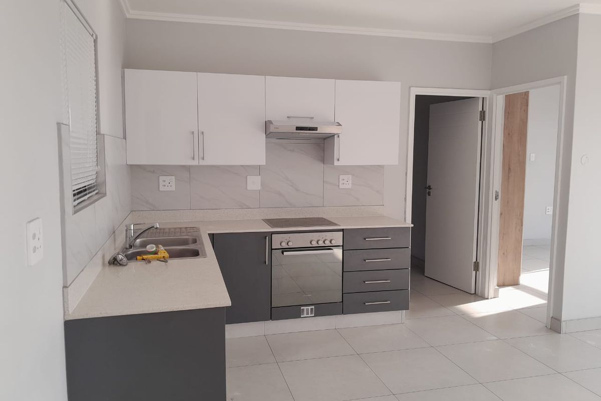 Modern kitchen featuring two-tone cabinetry, stone-look countertops, built-in oven, hob, and extractor fan, complemented by neutral floor tiles.
