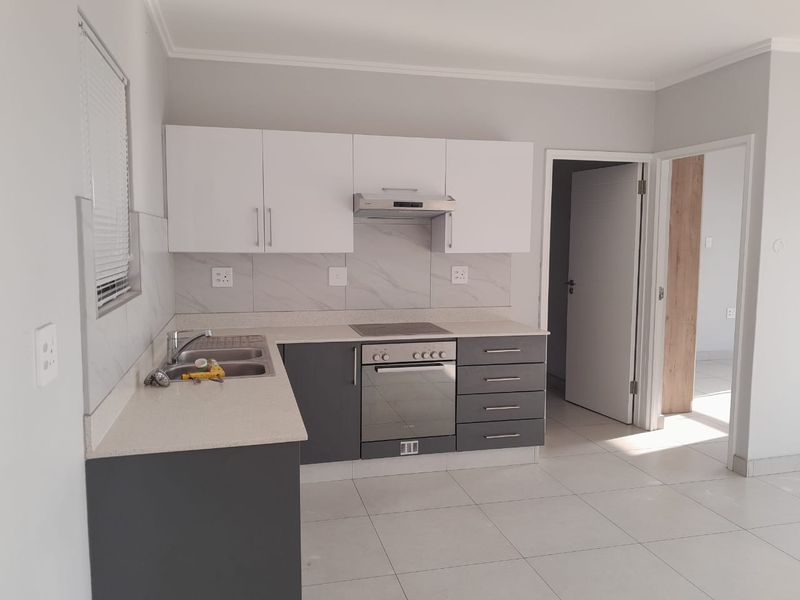 Modern kitchen featuring two-tone cabinetry, stone-look countertops, built-in oven, hob, and extractor fan, complemented by neutral floor tiles.
