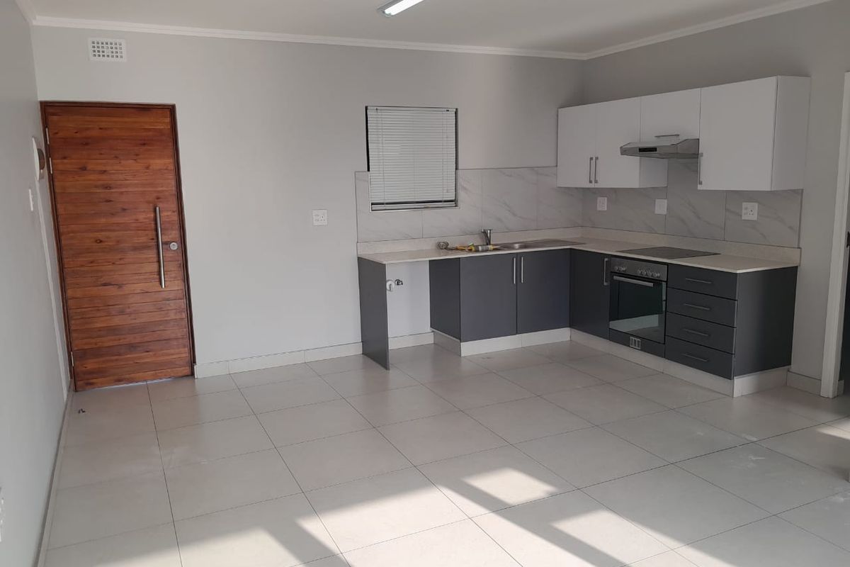Modern open-plan kitchen featuring two-tone cabinetry, integrated oven, hob, extractor fan, and tiled flooring in a bright, neutral living space.