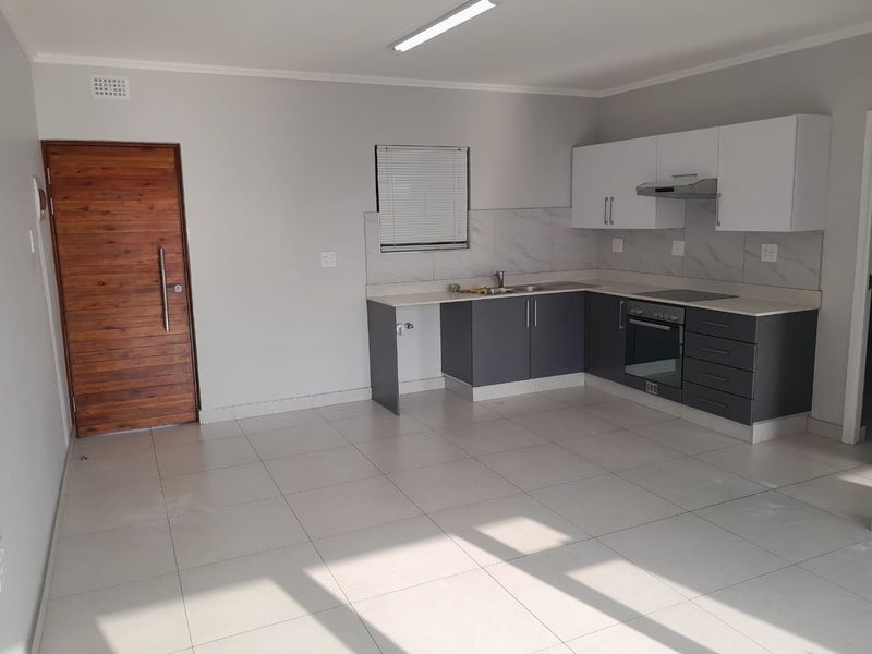 Modern open-plan kitchen featuring two-tone cabinetry, integrated oven, hob, extractor fan, and tiled flooring in a bright, neutral living space.