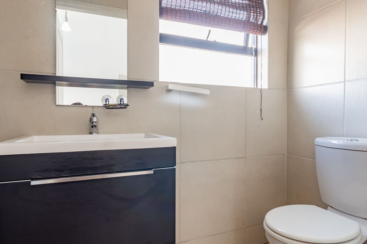 A compact bathroom featuring a modern vanity with integrated basin, wall-mounted mirror, and a standard toilet, finished with neutral wall tiling.