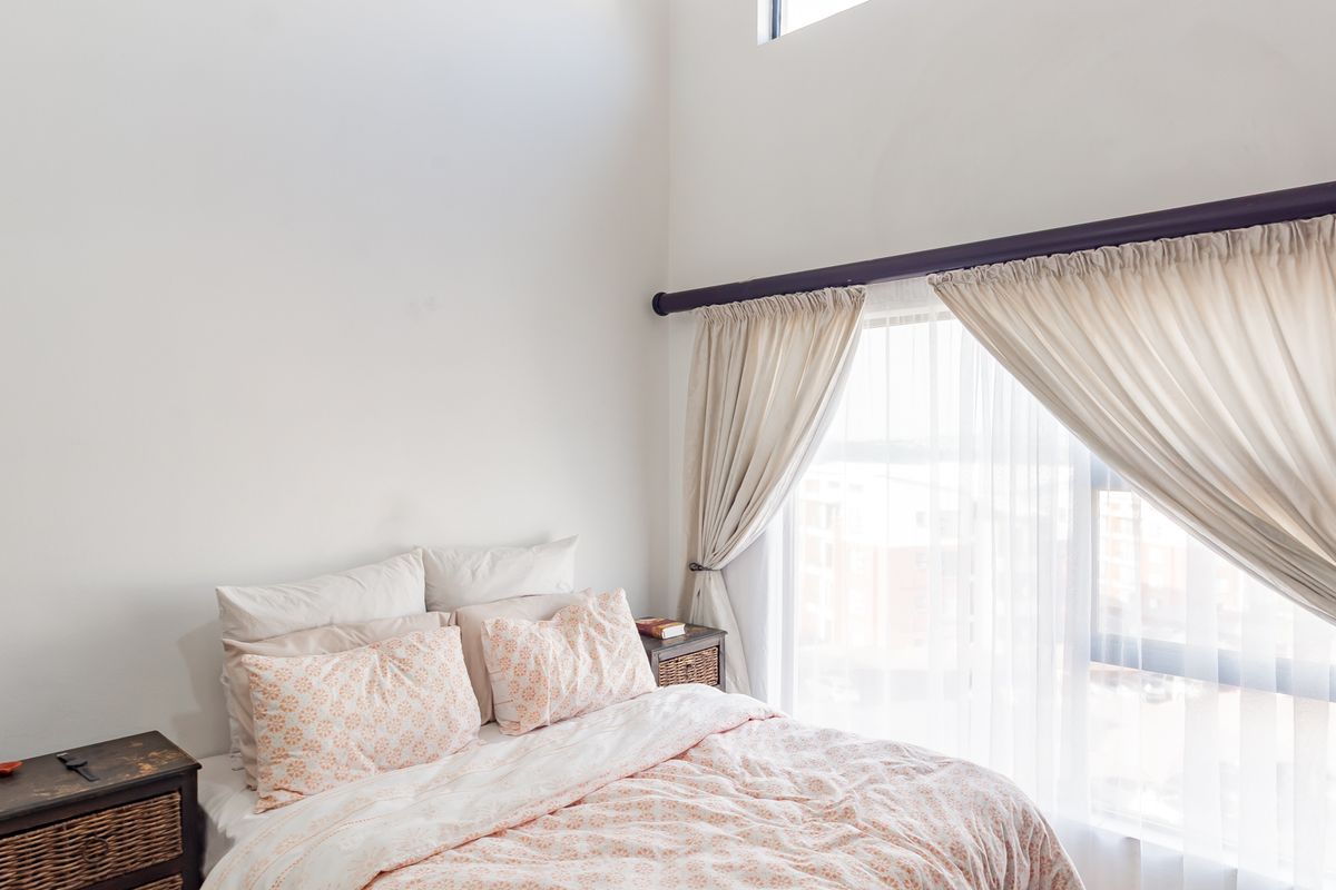 A bright bedroom featuring high ceilings, large windows with curtain tracks, and neutral wall finishes.
