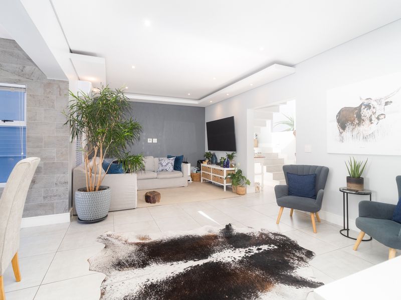 A bright and modern living room featuring a stone accent wall, recessed ceiling lighting, and neutral tiled flooring, leading to an internal staircase.