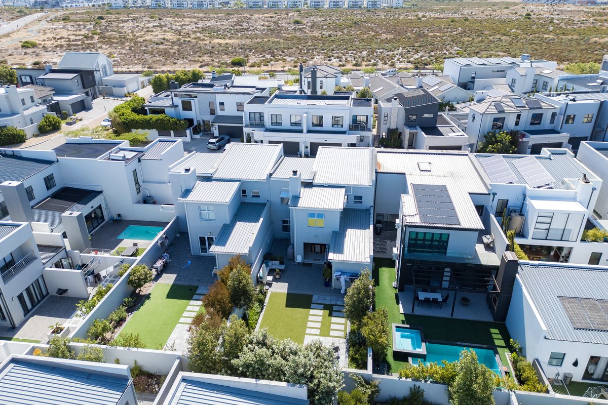 Aerial view of a modern residential estate featuring multiple homes with metal roofs, private swimming pools, and landscaped garden courtyards.