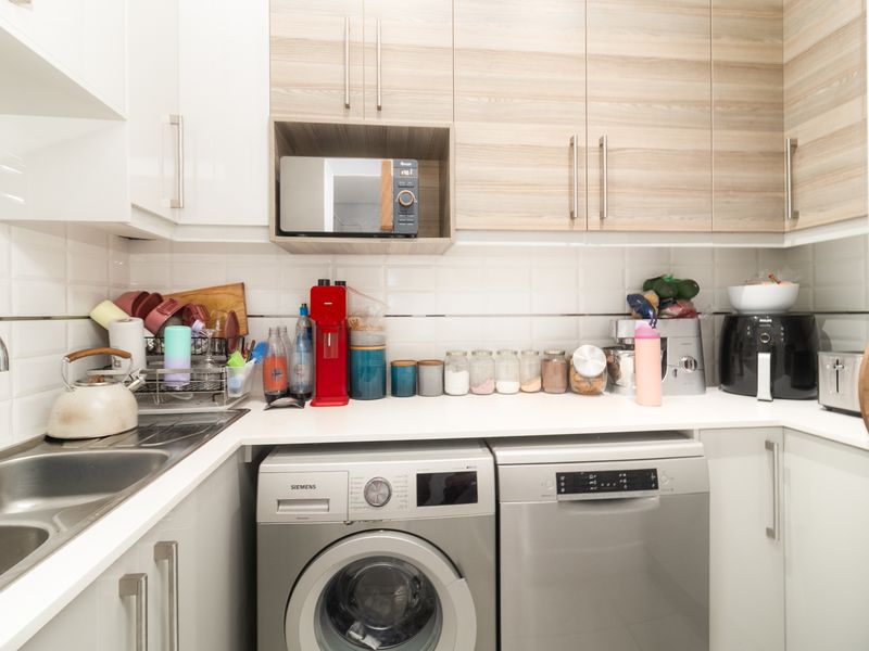 A functional scullery featuring modern cabinetry, subway tile backsplash, stainless steel sink, and integrated laundry and dishwasher appliances.