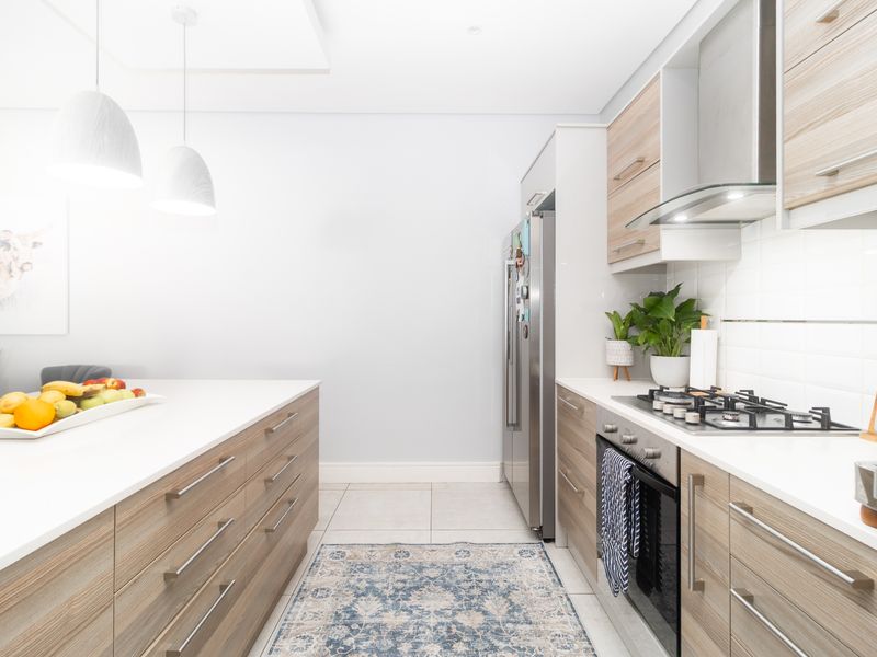 Modern kitchen featuring light wood cabinetry, stone countertops, a gas hob with extractor fan, and tiled flooring in a clean, contemporary layout.
