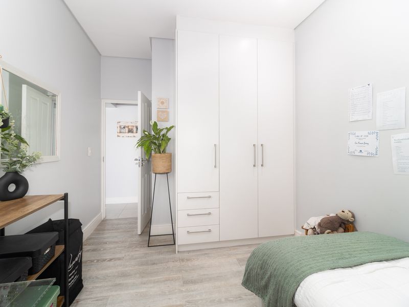 A well-maintained bedroom featuring light-toned laminate flooring and a modern, white built-in wardrobe with ample storage space.