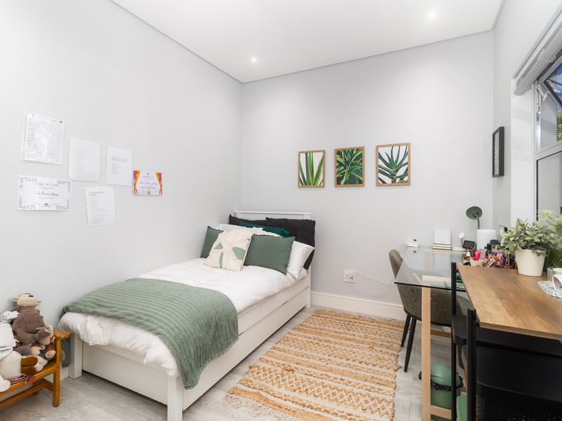 A well-maintained bedroom featuring neutral walls, recessed downlighting, and modern aluminium window frames, providing a bright and functional living space.