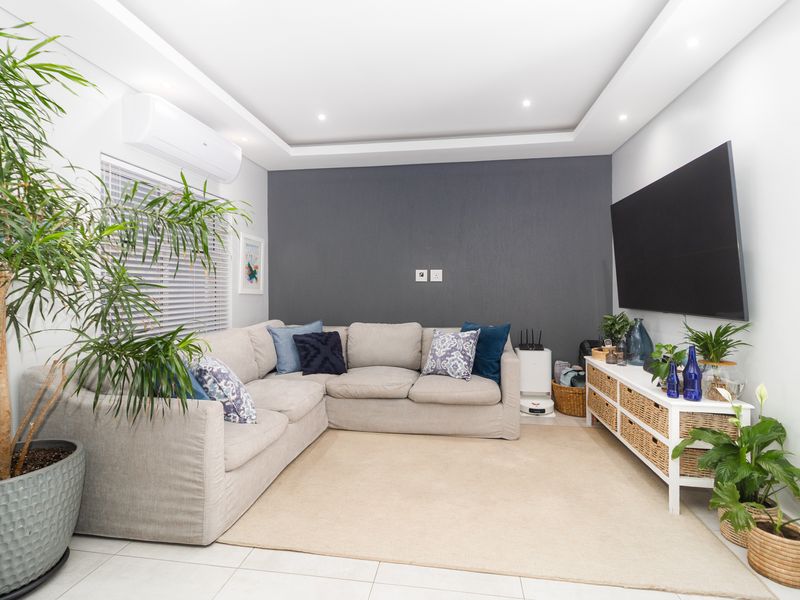 A well-maintained living room featuring tiled flooring, a recessed ceiling with downlights, and a wall-mounted split-system air conditioner.
