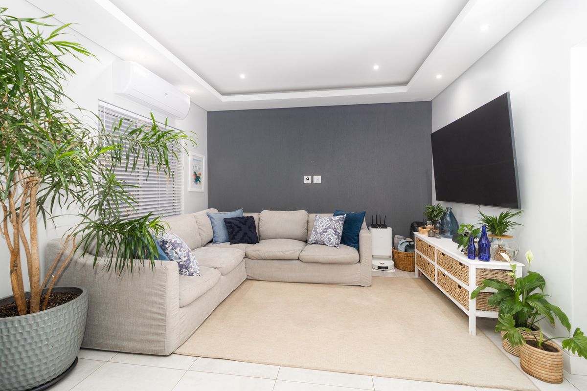 A well-maintained living room featuring tiled flooring, a recessed ceiling with downlights, and a wall-mounted split-system air conditioner.