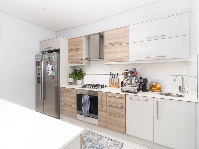 Modern kitchen featuring two-tone cabinetry, stone countertops, gas cooktop, built-in oven, stainless steel extractor fan, and a tiled backsplash.