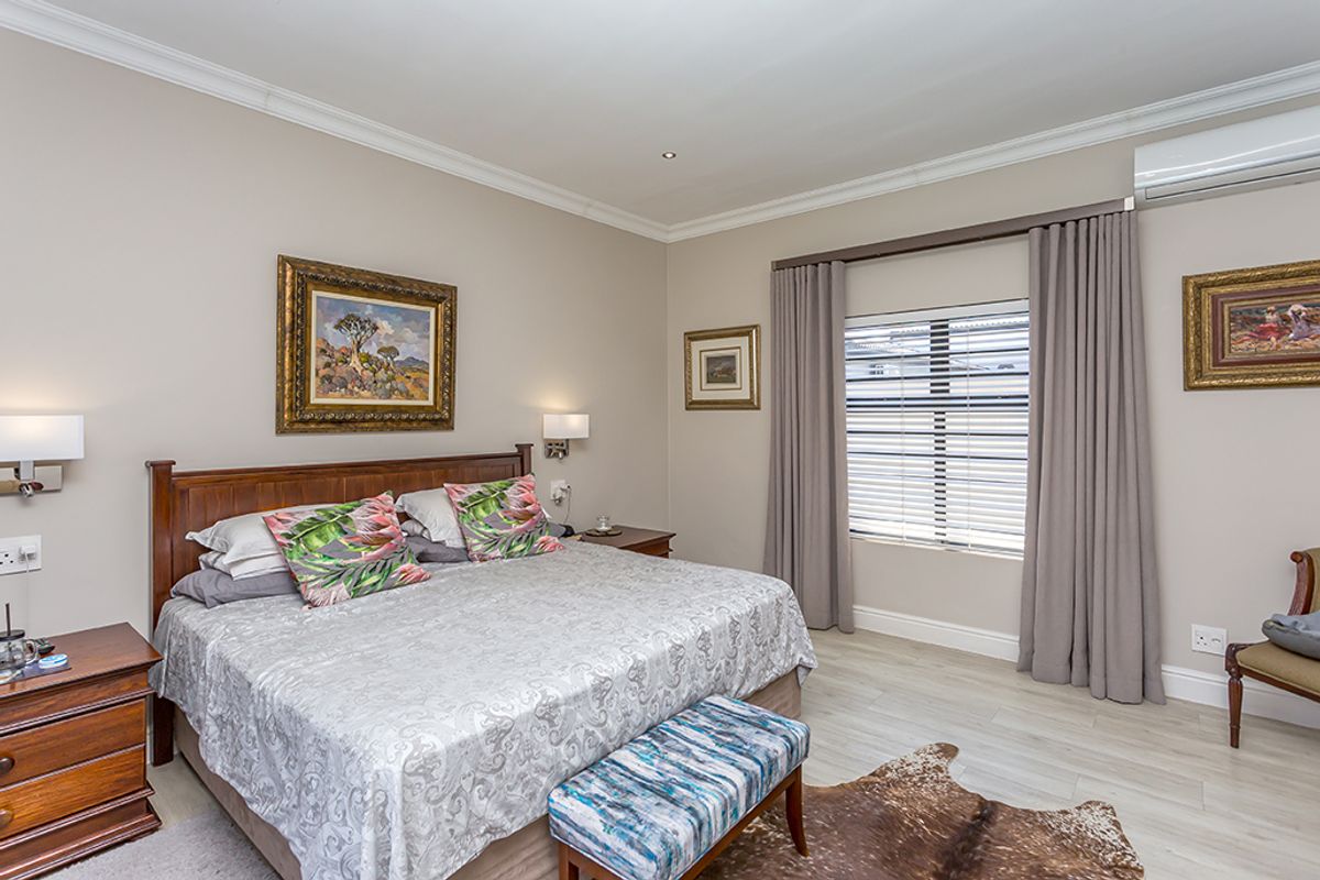 A well-maintained bedroom featuring light-toned flooring, crown molding, wall-mounted lighting, and a split-system air conditioning unit.