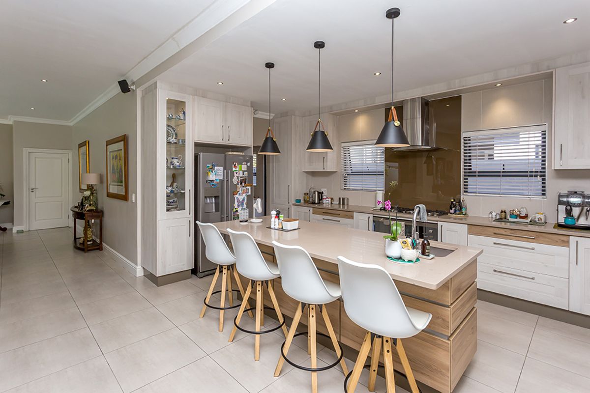 Modern open-plan kitchen featuring a large central island with breakfast bar seating, integrated cabinetry, stone countertops, and contemporary pendant lighting.