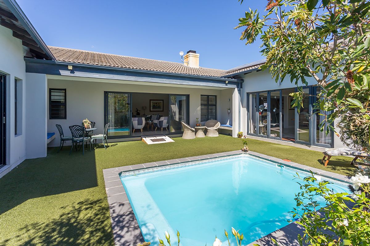 A private rear courtyard featuring a swimming pool, artificial lawn, and covered patio area with seamless indoor-outdoor flow through sliding glass doors.