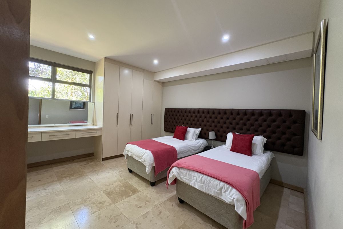 Spacious bedroom featuring built-in cupboards, a vanity area with mirror, recessed downlighting, and tiled flooring.