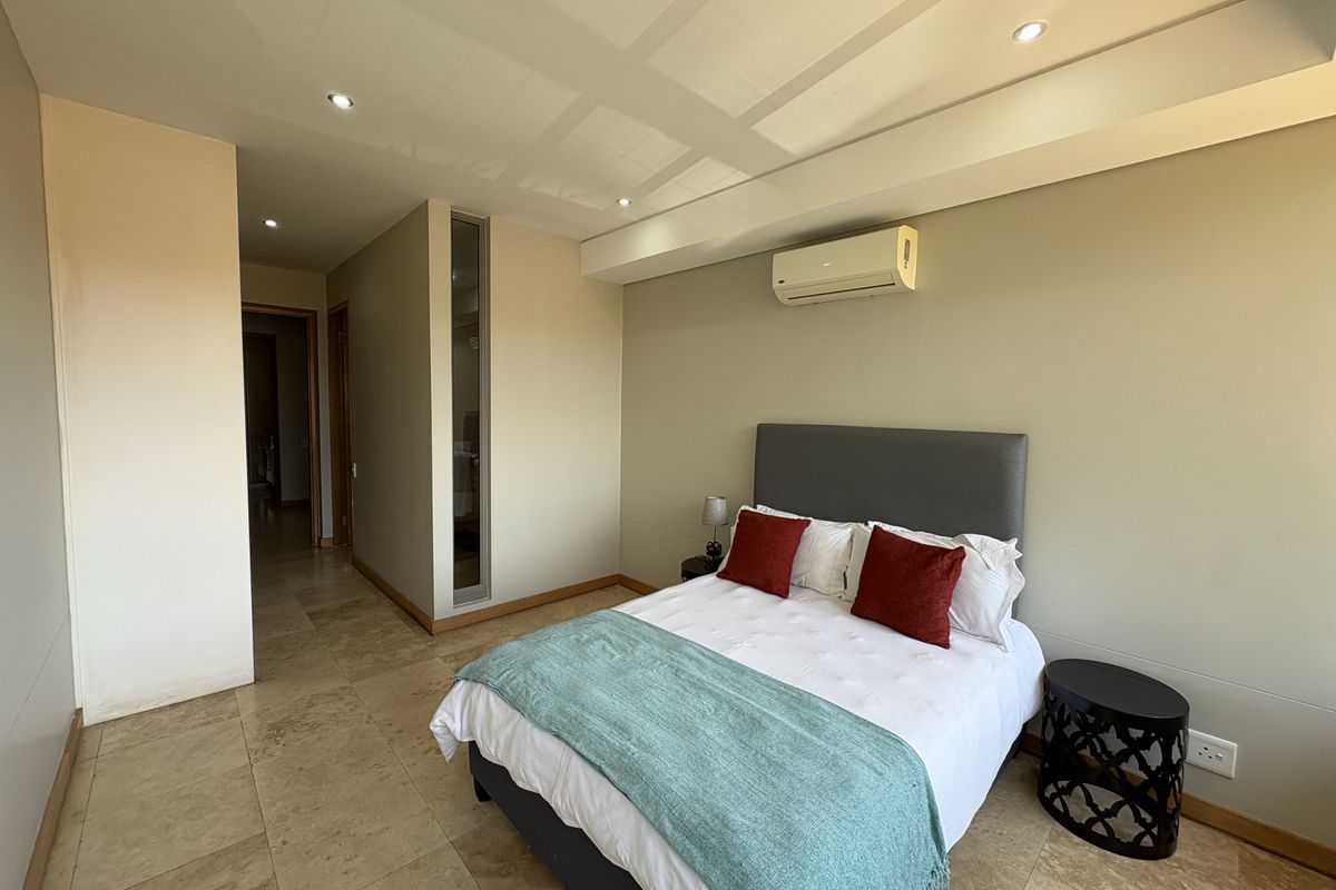 A well-maintained bedroom featuring tiled flooring, recessed ceiling lighting, and a wall-mounted air conditioning unit.