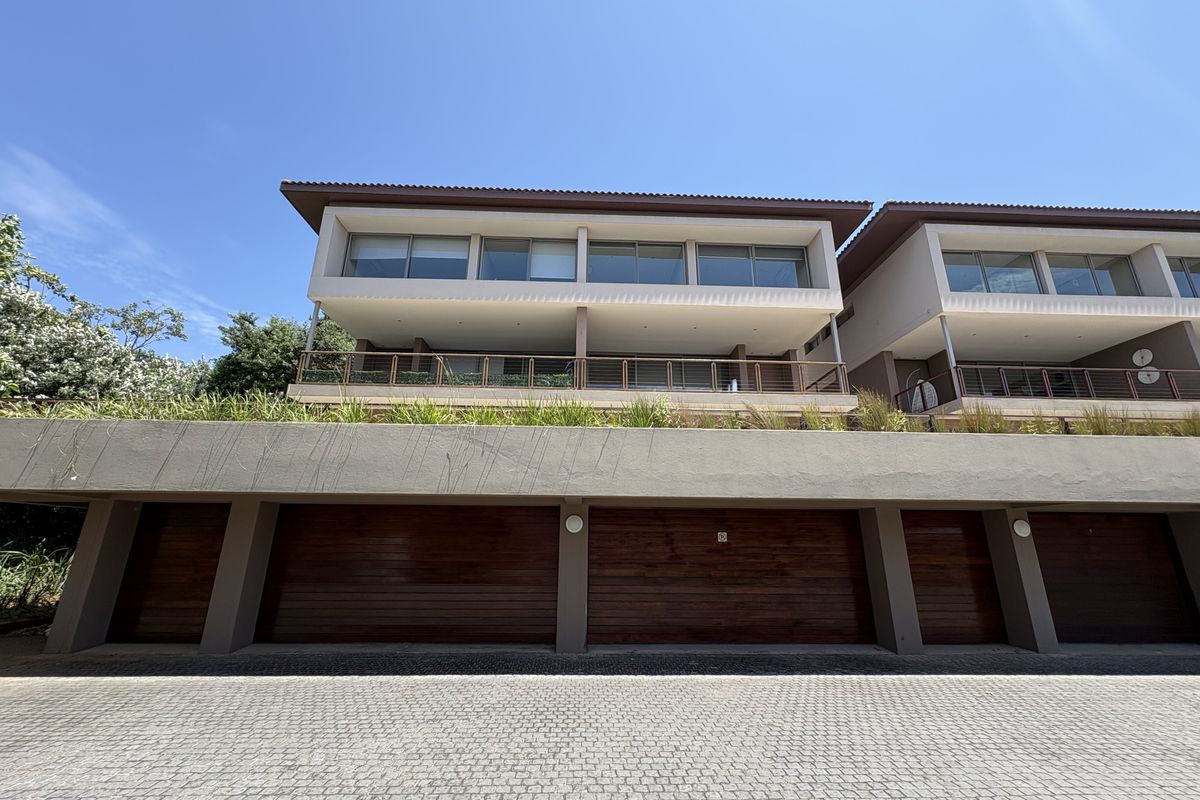 A modern multi-level residential building featuring a paved driveway, integrated timber-finish garage doors, and upper-level balconies with glass balustrades.