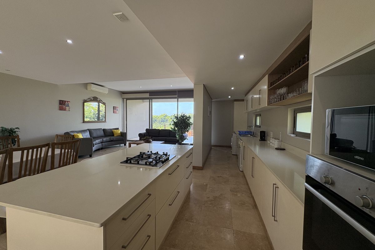Spacious open-plan living area featuring a modern kitchen with a central island, gas hob, and stone countertops, flowing seamlessly into the lounge and patio.