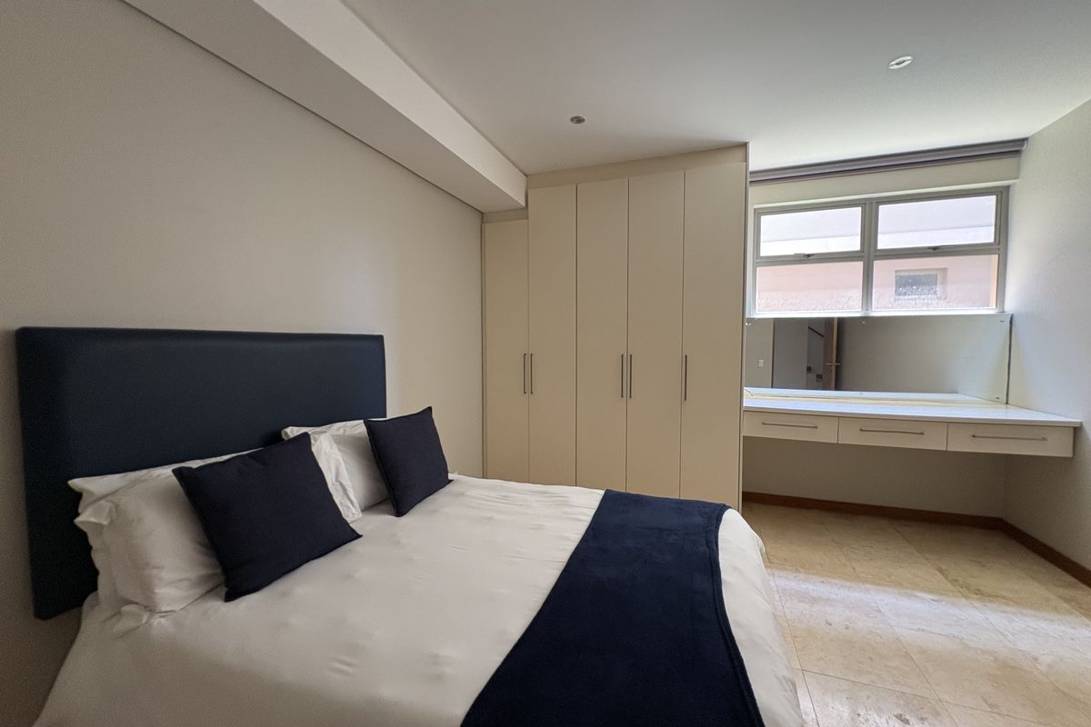 A well-lit bedroom featuring built-in cupboards, a vanity area with a mirror, and tiled flooring.