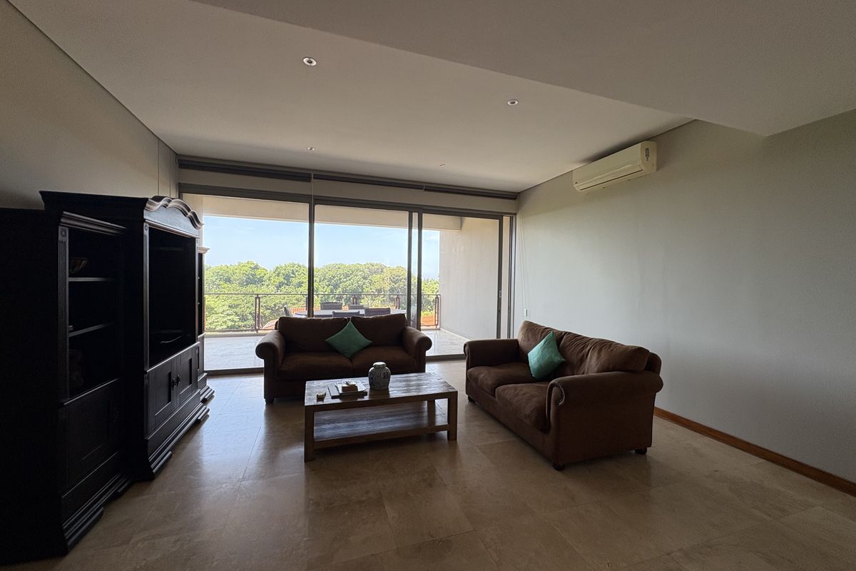 Spacious living room featuring large sliding glass doors that open onto a balcony, tiled flooring, and a wall-mounted air conditioning unit.