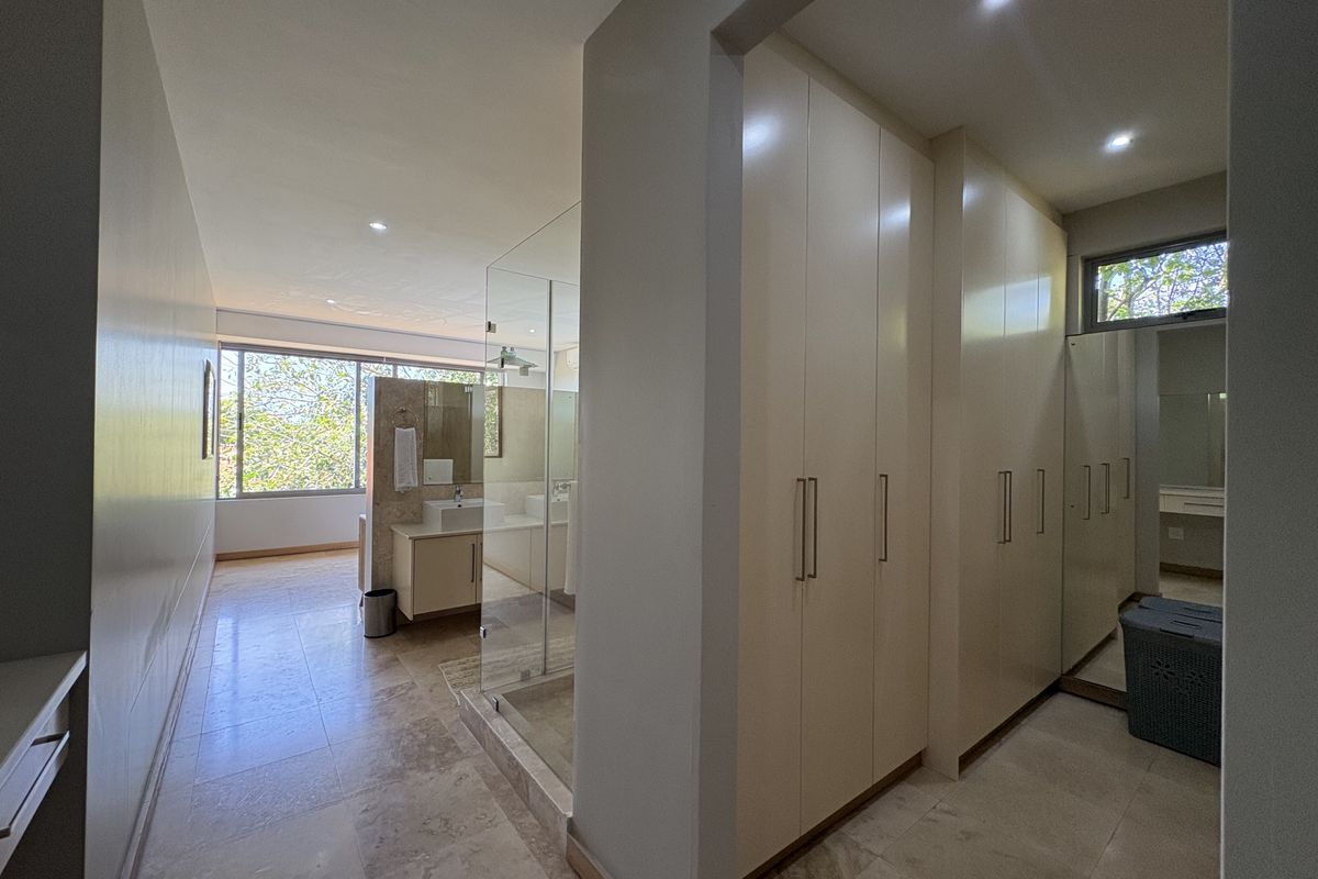 Spacious en-suite bathroom featuring a glass-enclosed shower, modern vanity, and extensive built-in cabinetry for ample storage.